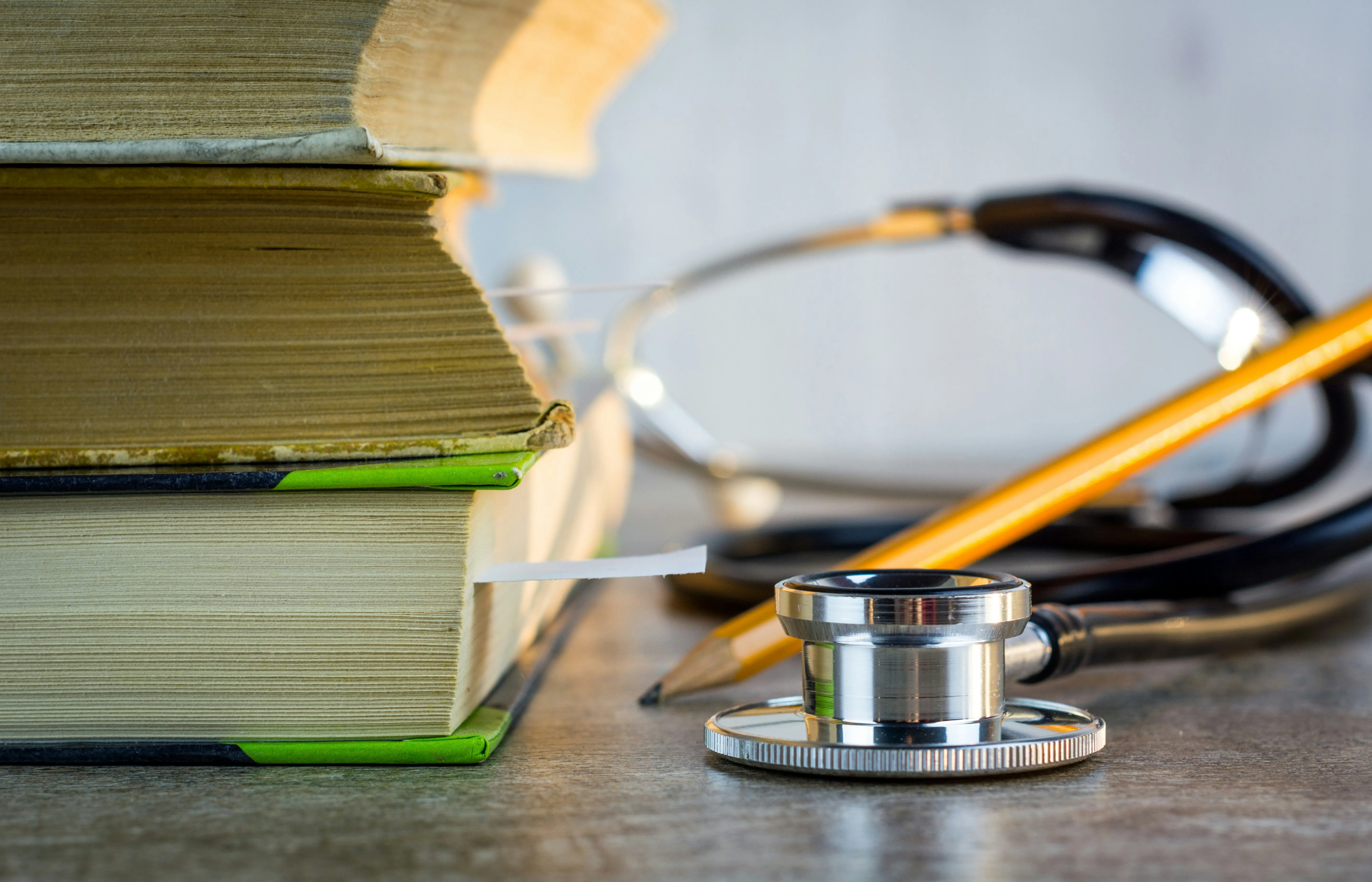 Stacked books beside a stethoscope and pencil