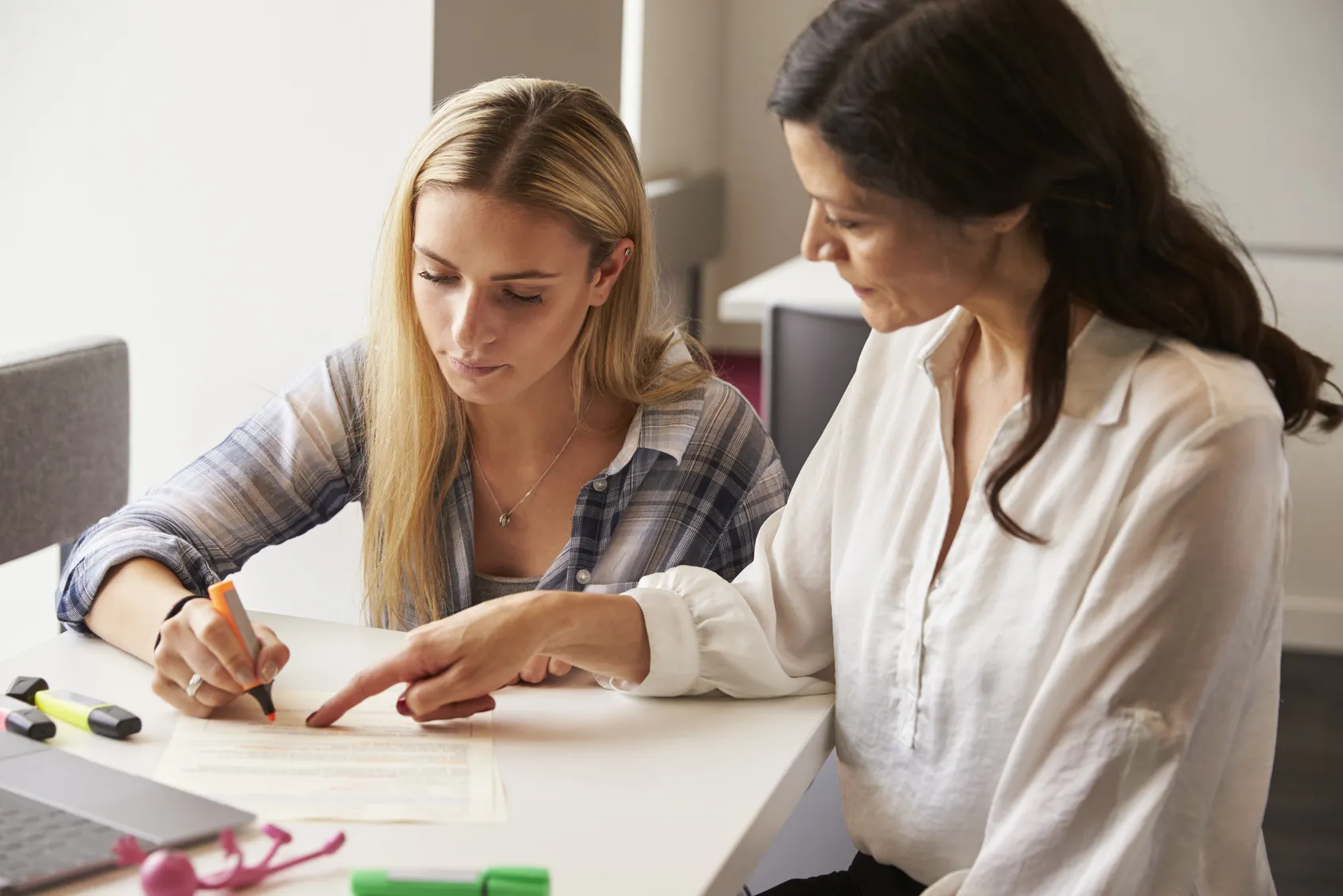 A woman writing at a desk while another person watches