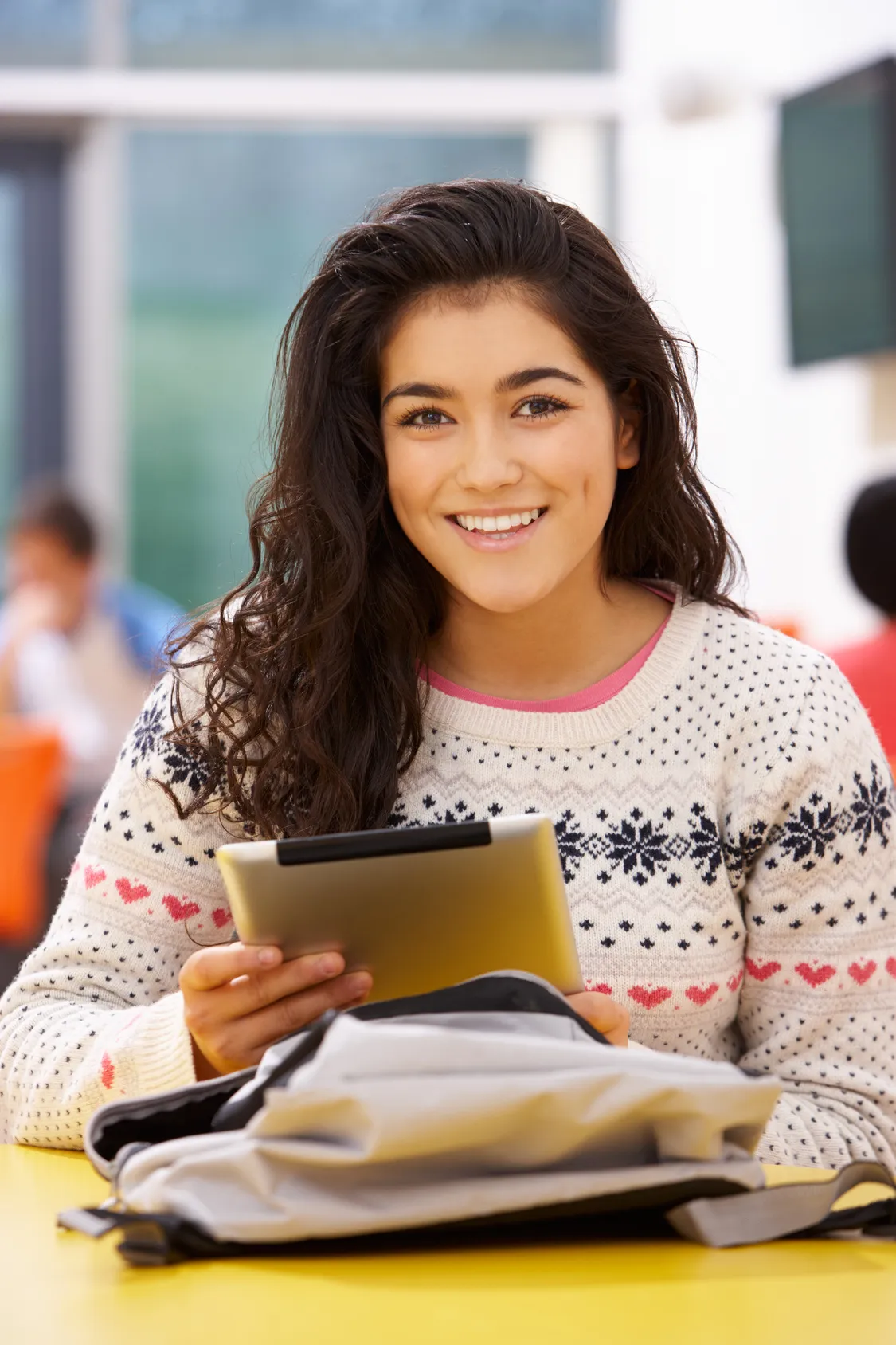 A smiling student with a tablet and backpack at a desk
