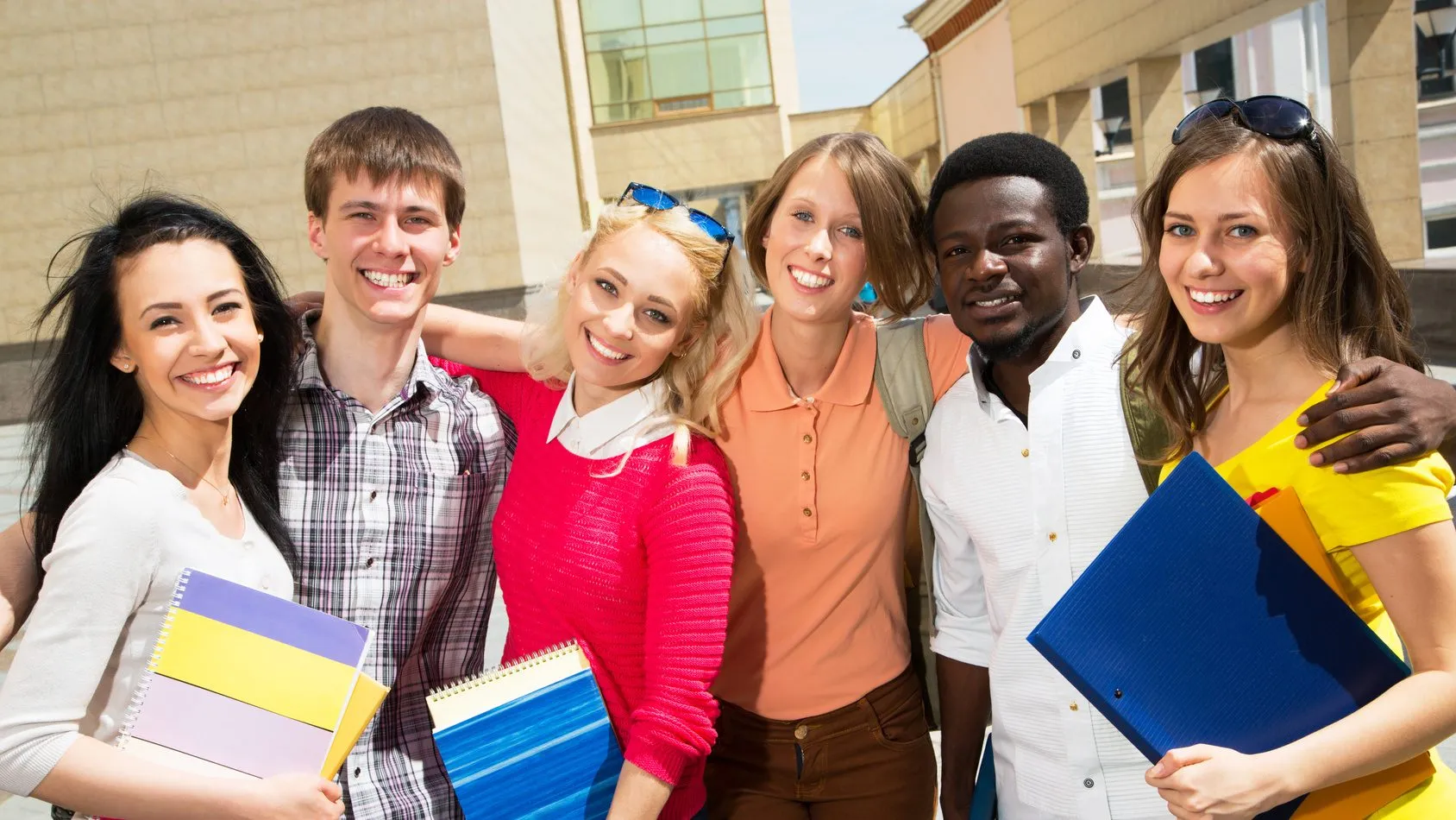 Six students smiling together outdoors in front of a campus building