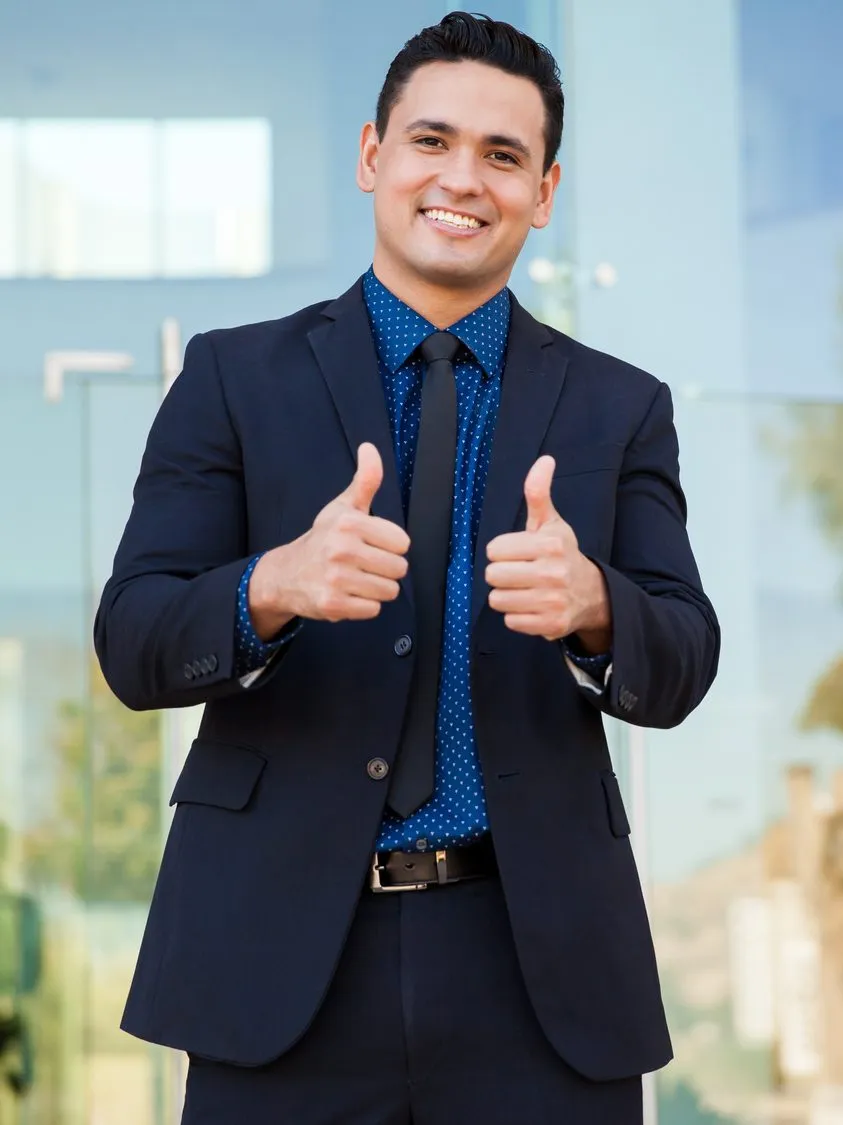 A smiling man in a navy suit giving two thumbs up