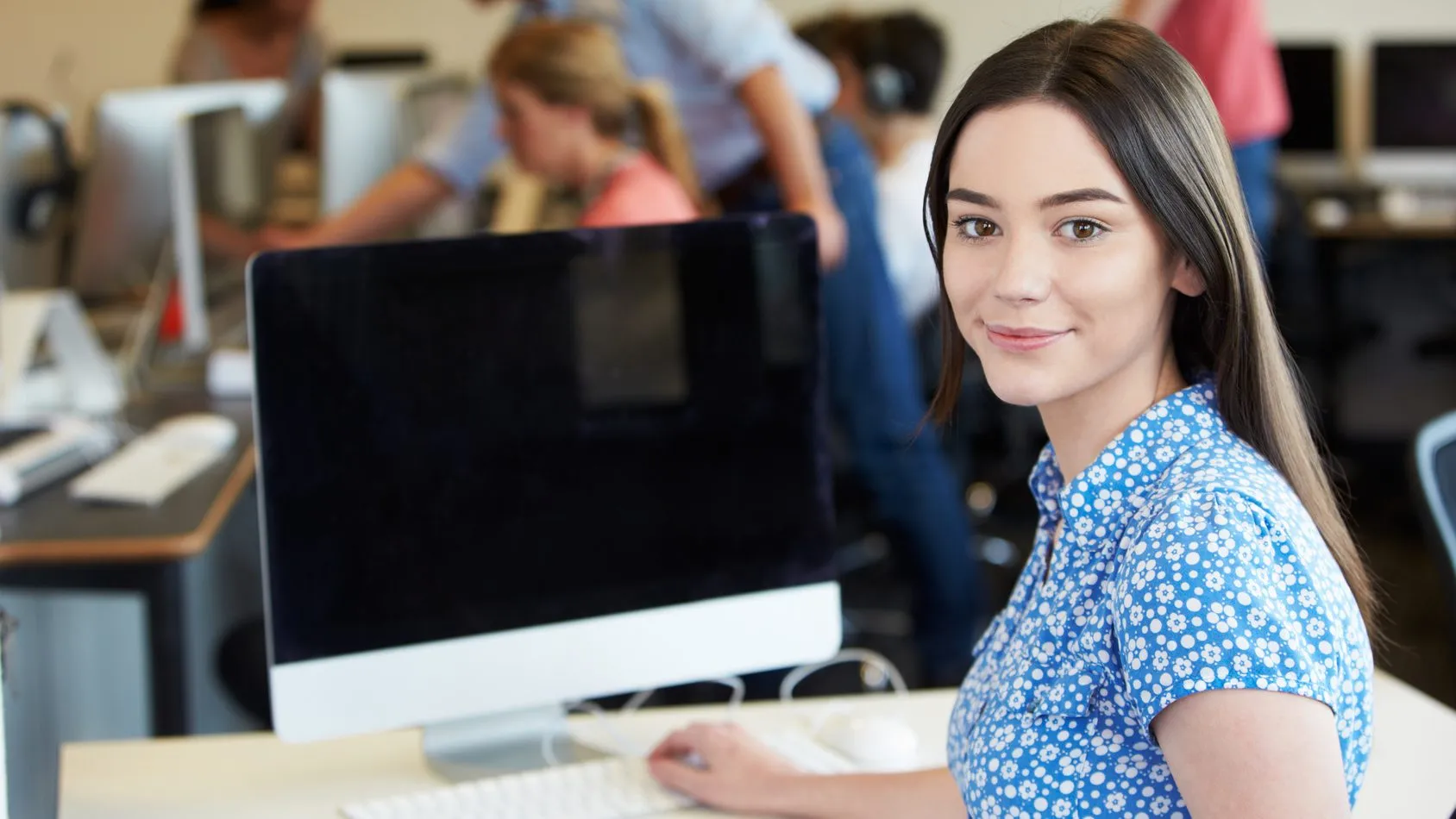 Smiling woman in a blue floral blouse working at a computer