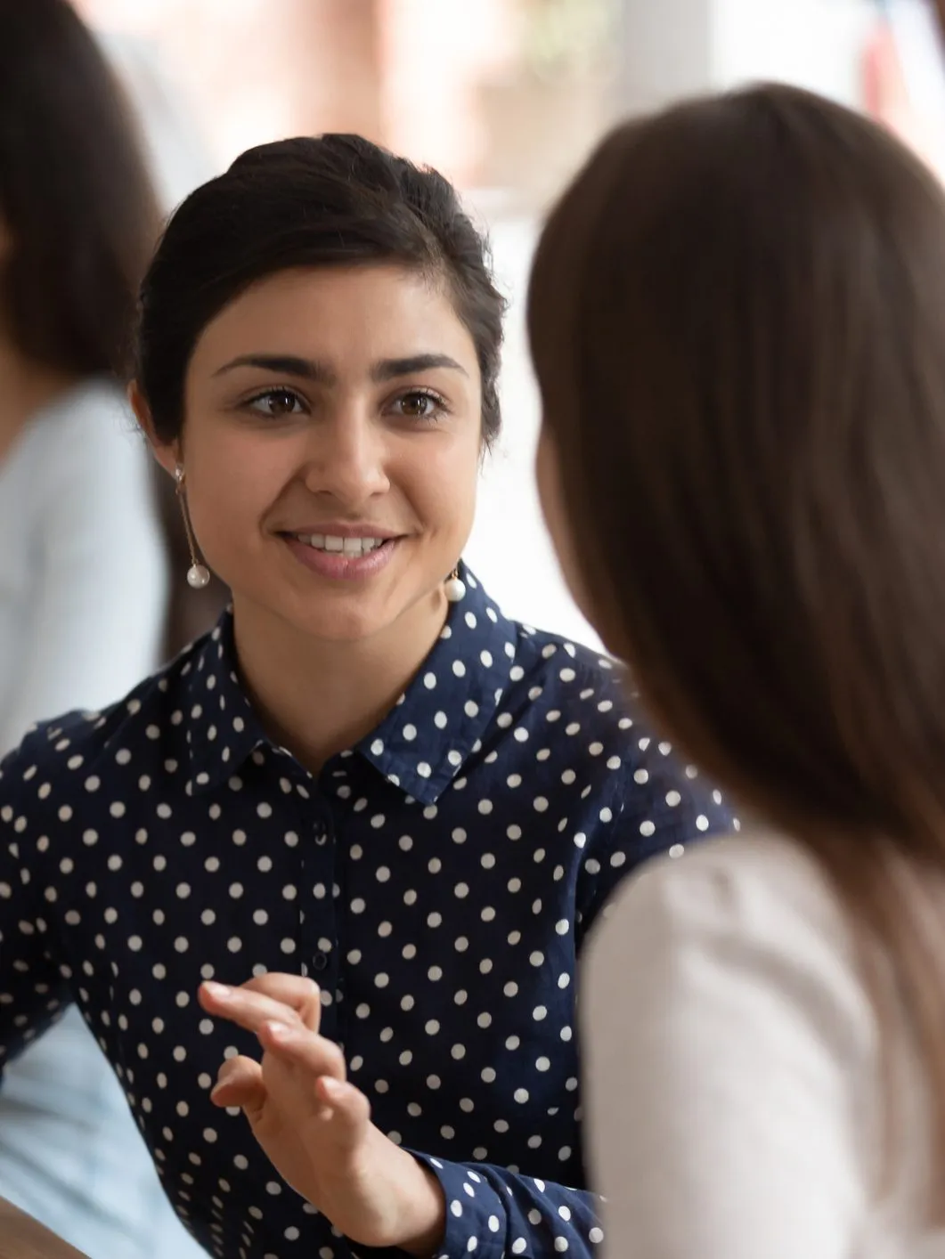 Smiling young woman in a navy polka-dot blouse talking with a classmate