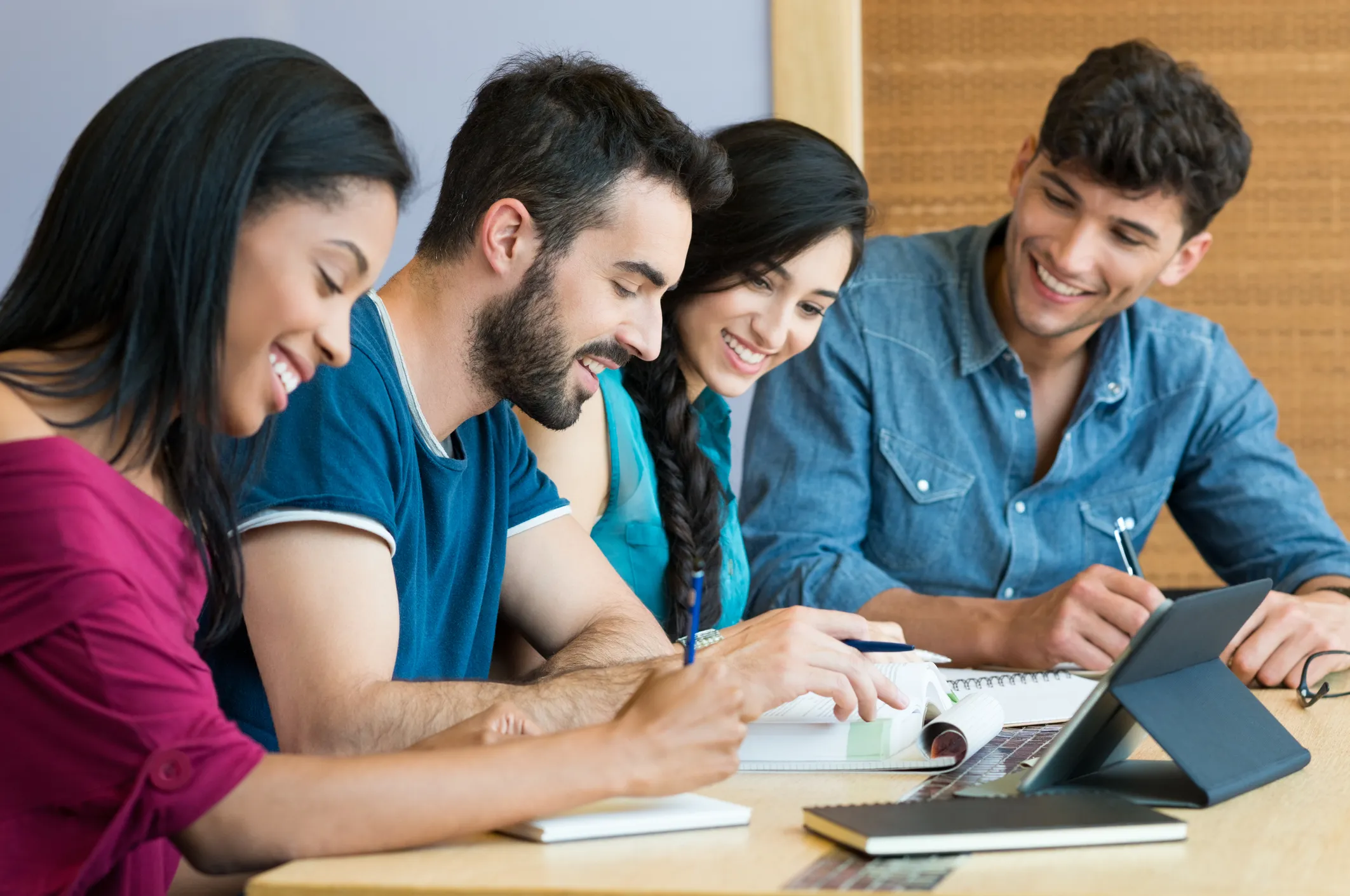 Four smiling students studying together at a table with a tablet and notebooks