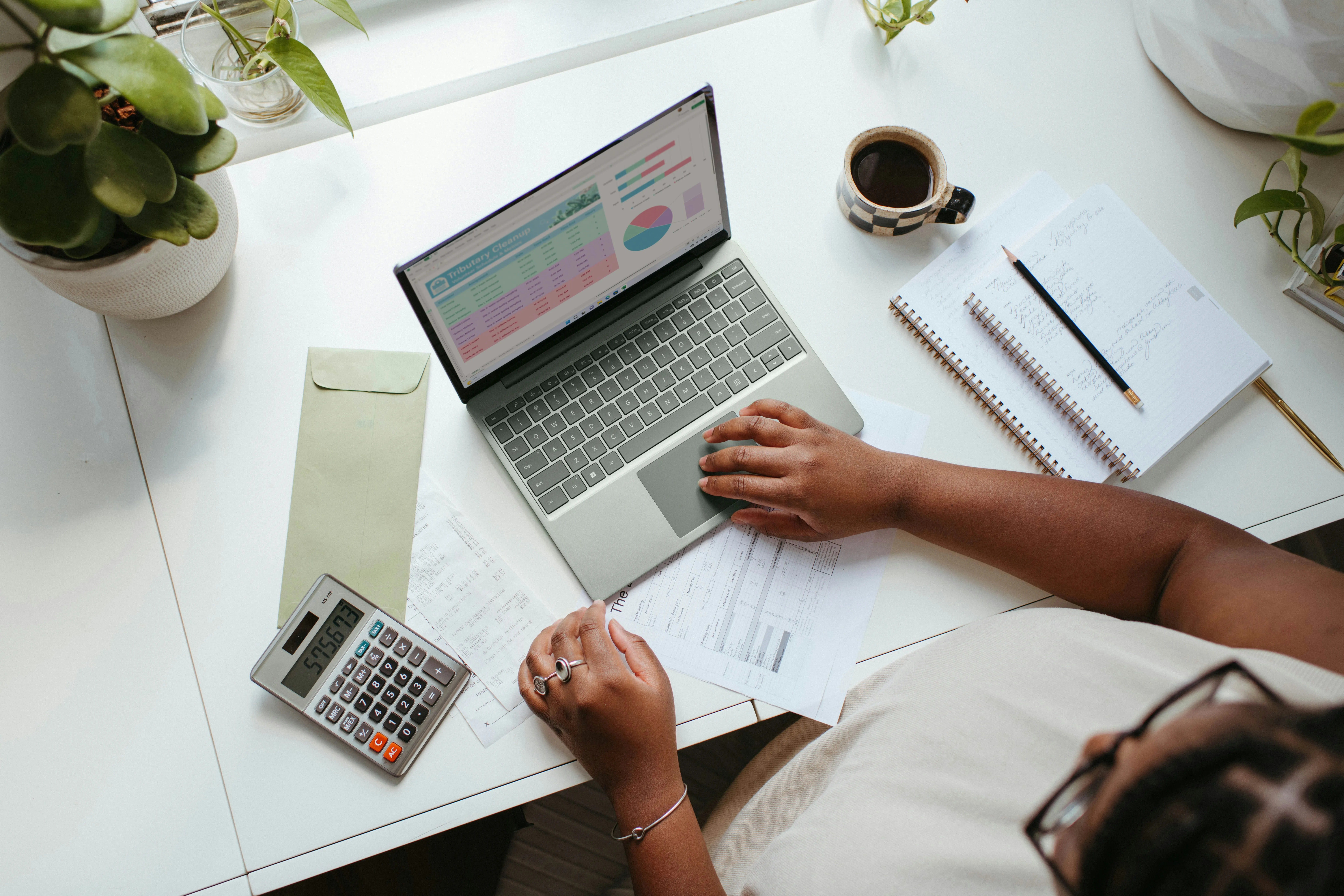 A desk with a laptop, calculator, coffee and notebook