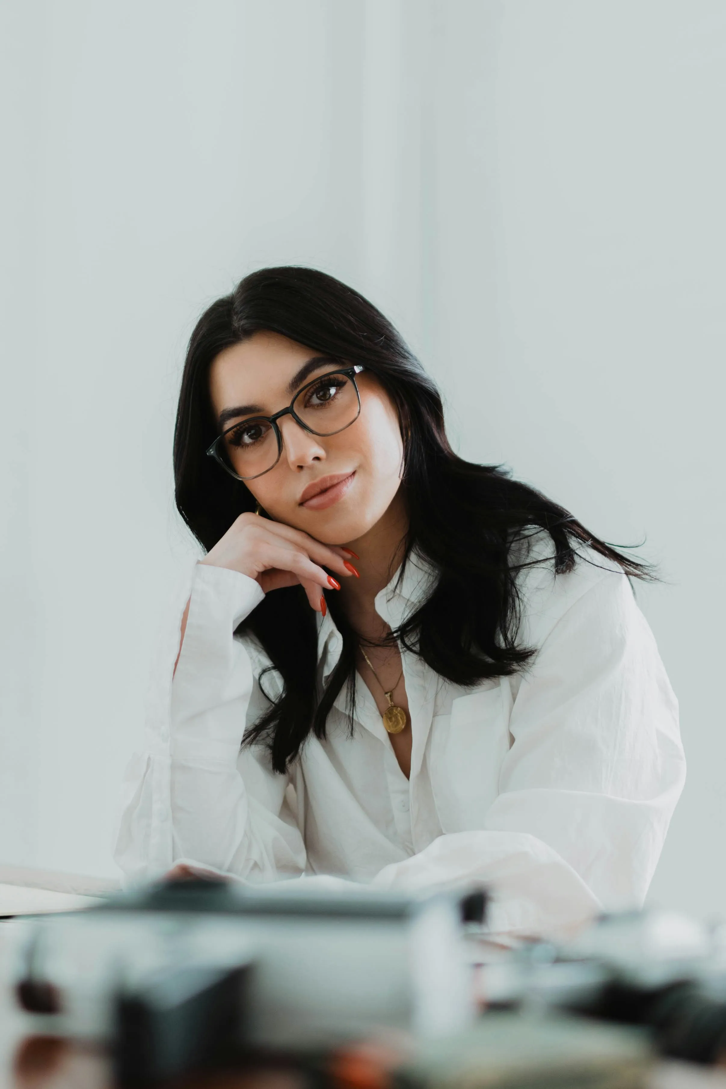 A young woman with glasses resting her chin on her hand at a desk